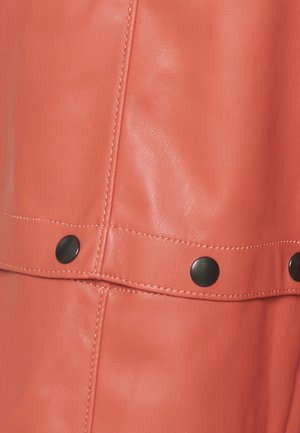 Gros plan sur un cuir de couleur corail avec une couture verticale et horizontale et des boutons-rivets ronds noirs sur la couture horizontale.