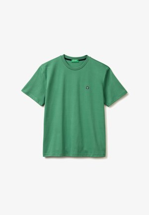 Zielona koszulka z krótkim rękawem i okrągłym dekoltem z małym czarno-białym logo na lewej piersi, wyświetlana na białym tle.