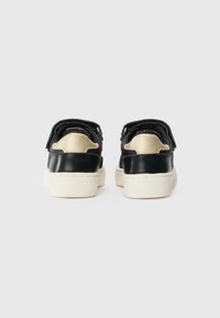Sneaker in tessuto nero con tallone nero liscio e dettagli beige, dotati di fasce regolabili e suola testurizzata e imbottita.