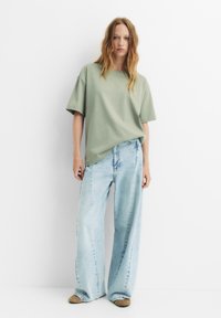 Overgrote olijfgroene katoenen t-shirt gecombineerd met lichtblauwe wijde jeans. Zachte textuur, casual ontwerp, minimale accenten.