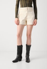 Cream-colored cotton shorts with braided waistband, paired with black leather cowboy boots featuring intricate stitching and pointed toes.