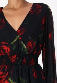 Abito nero con stampa floreale rossa e verde; presenta un collo a V, maniche lunghe e una vita arricciata. Realizzato in tessuto leggero.