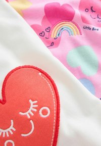 Prikazana sta dva kosa blaga. Eden je bel z rdečim vezenim srcem; drugi je roza s pisanimi srci in mavričnim vzorcem.