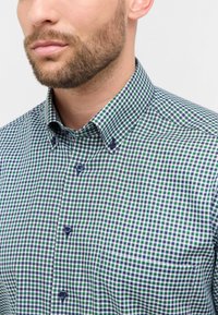 Groen en blauwe geblokte overhemden met een button-down kraag. Bevat kleine knopen en een borstzak. Katoenen stof, gladde textuur.
