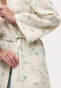 Accappatoio di tessuto waffle beige chiaro con stampe a tema spiaggia in tonalità teal, comprese conchiglie e uccelli, dotato di una tasca frontale e cintura abbinata.