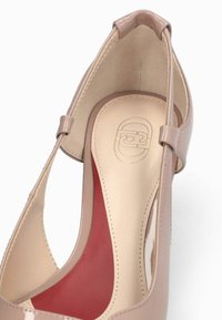 Chaussure slingback en cuir verni beige avec semelle intérieure rembourrée présentant un logo embossé et un détail de soutien de la voûte plantaire en rouge.