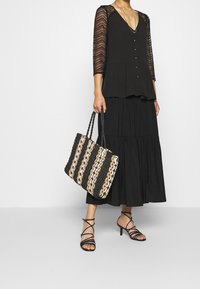 Černý peplum top s krajkovými rukávy, doplněný o vrstvenou černou sukni. Woven tote má černé, zlaté a bílé pruhy; páskové černé podpatky.