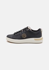 Black sneakers with a textured leather upper, gold eyelets, a round logo on the side, and a white rubber sole accentuated with a gold strip.