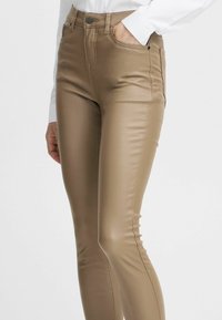 Leggings en simili cuir beige présentant une coupe slim, une taille haute et des poches latérales ; texture lisse avec un minimum de coutures.