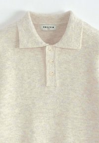 Polo en tricot de couleur crème avec une texture douce, doté d'une patte de boutonnage à deux boutons et d'un col rabattable. L'étiquette indique "FRILIVIN".