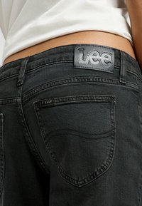 Vaqueros de mezclilla negra con un parche de cuero con la marca en la parte posterior, detalles de costura sutil y un diseño clásico de bolsillo trasero.