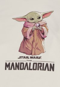 Cartoonfiguur met grote oren, gekleed in een roze-bruin gewaad, met een kleine bol in de hand; onderaan de tekst staat "Star Wars The Mandalorian."