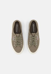 Olivenfargede kanvas sneakers med hvite gummisåler, som har runde lisser, forsterkede lisseholdere og en logo på tungen.
