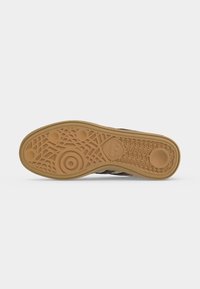 Σόλα ενός καφέ sneaker Adidas με κυκλικά και πλέγμα σχέδια πέλματος και το λογότυπο Adidas κοντά στην καμάρα.