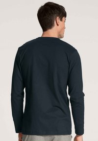 Een donkerblauwe longsleeve-shirt van katoen, met een ronde halslijn en een gladde textuur, recht afgewerkt aan de onderkant en met minimale details.