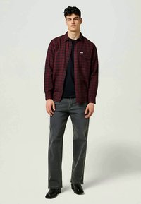 Punase ja musta ruudulise mustriga pikkade varrukatega särk, ees nööbitav ja ühe rinnataskuga, kantud musta t-särgi ja hallide teksade peal.