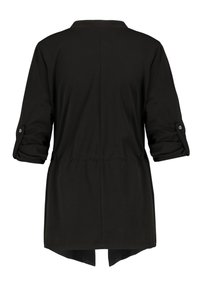 Veste longue noire à manches longues retroussées fixées par des pattes à boutons, taille cintrée et ourlet arrière légèrement plus long, vue de dos.