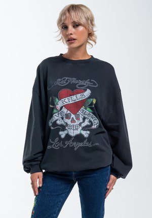 Felpa nera oversize con una grafica di teschio colorata, caratterizzata da un cuore rosso, foglie verdi e testo bianco. Maniche lunghe con polsini a coste.
