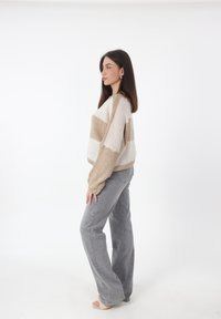 Beige en crème gestreepte trui met een relaxte pasvorm en ribbelstructuur, gecombineerd met hoogwatergrijze jeans en sandalen. Eenvoudige achtergrond.