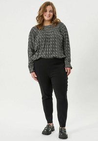 Černobílá vzorovaná blůza s dlouhým rukávem a nařaseným výstřihem, spárovaná s černými slim-fit kalhotami a robustními černými botami.