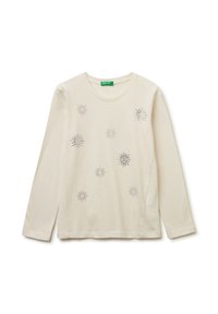 Helle beige Langarmbluse aus weichem Baumwollstoff mit dekorativen silbernen Verzierungen, die Sterne ähneln, mit rundem Halsausschnitt und Seitenschlitzen.