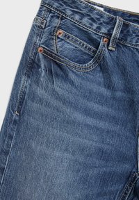 Närbild på blå denimjeans fram med synlig myntficka, bältesögla och kopparnitar på övre vänstra sidan.