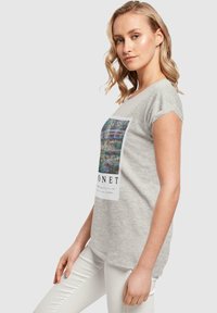T-shirt grise à manches courtes avec une impression d'œuvre de Monet à l'avant, dotée d'un col rond et d'une coupe légèrement décontractée.