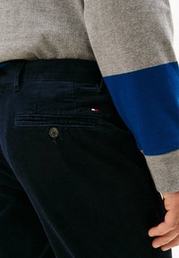 Pantaloni in velluto a coste blu navy con una finitura testurizzata, dotati di una tasca posteriore e un piccolo logo rosso, bianco e blu. Maglia a maniche lunghe grigia e blu.