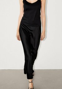 Sorte satin tanktop kombineret med sorte satinbukser. Bukserne har en afslappet pasform med en glat tekstur. Modellen bærer stilige sandal med remme.