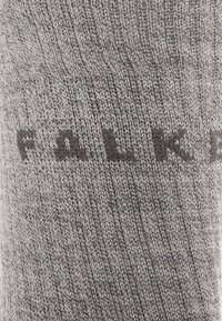 Calcetín de punto gris con una textura suave y un empeine que presenta el nombre de la marca "FALK" en letras gris oscuro.