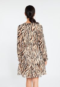 Vestido de manga corta en una tela ligera y transparente, con un patrón de rayas de tigre en beige, negro y naranja, y un dobladillo con volantes.