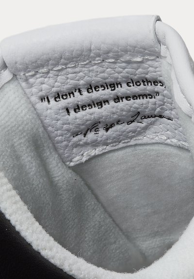 Nahaufnahme der weißen Schuhzunge mit Lederpatch, der das Zitat "I don't design clothes, I design dreams." und die Unterschrift von Ralph Lauren zeigt.