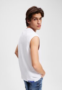 Tricou fără mâneci, alb, din bumbac, cu decolteu rotund și cusături vizibile. O etichetă albastră cu "KARL LAGERFELD" pe tiv.