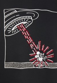 Svart tyg med vitt och rött broderi av en UFO med en stråle och en figur som står nedanför. Texturerade paljetter framhäver designen.