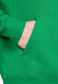 Grüne Sweatshirt mit einer Seitentasche, gerippten Bündchen und weichem Baumwollstoff, der eine einheitliche Textur und lebendige Farbe zeigt.