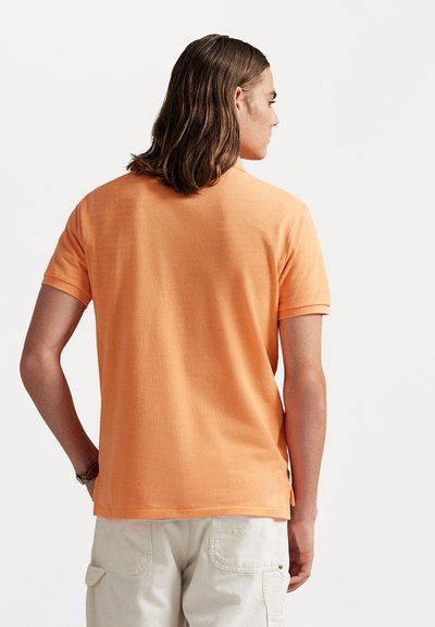 Κοντομάνικη, πορτοκαλί πολο μπλούζα από μαλακό ύφασμα, με κλασικό γιακά, πλαϊνές σχισμές και υφή που προσφέρει άνεση.