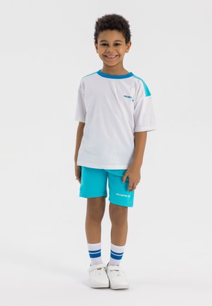 Youth sports outfit featuring a white short-sleeved t-shirt with blue accents and turquoise shorts; includes white sneakers and striped socks.