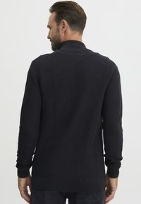 Fekete kötött pulóver bordás textúrával, hosszú ujjakkal és magas gallérral. Egyszerű dizájn, egyenes szegéllyel rendelkezik.