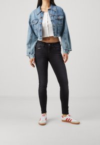 Chaqueta de mezclilla recortada en azul claro con cierre de botones, combinada con jeans ajustados negros y zapatillas blancas con rayas y acentos rojos.