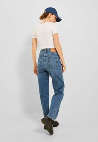 Jeans in denim blu con una vestibilità ampia, vita media e due tasche posteriori. Abbinati a una camicia bianca attillata e a un cappellino da baseball blu.