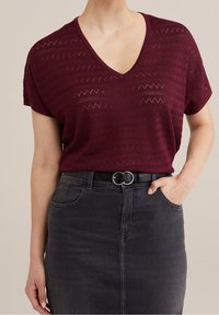 Bordeaux gebreid topje met een V-hals en korte mouwen, gecombineerd met een grijze denimrok en een zwarte riem met een zilveren cirkelvormige gesp.