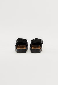 Sandales noires à dos ouvert avec des sangles réglables, en tissu noir texturé, semelle en liège et semelle en caoutchouc flexible.