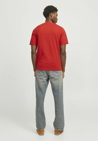 Camiseta de algodón roja con mangas cortas y cuello redondo, combinada con vaqueros de denim de pierna ancha en azul claro y calzado marrón. Ajuste casual en general.