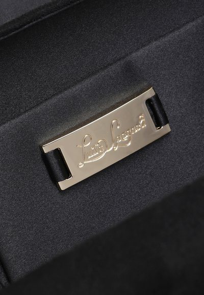 Guldmetalplade med logoet "Luisa Spagnoli" i skrift, fastgjort til sort stof, sandsynligvis indeni en håndtaske eller tilbehør.