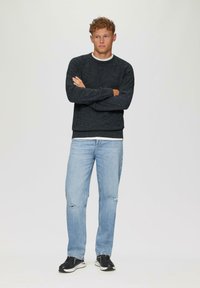 Donkergrijze trui van textiel met een gestructureerde stof, ronde halslijn en geribde manchetten, gecombineerd met lichtblauwe ripped jeans en zwarte sneakers.