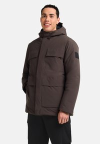 Brauner isolierter Parka mit Kapuze, ausgestattet mit zwei Brusttaschen und Seitentaschen. Glatte Textur und ein schwarzes Logo-Patch am Ärmel.