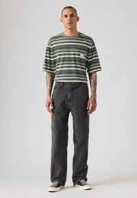 Camisa de manga corta a rayas verdes y grises con un bolsillo, combinada con unos vaqueros rectos grises y unas zapatillas blancas y negras.