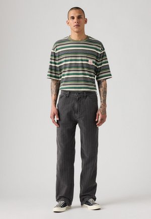 Chemise à manches courtes rayée verte et grise avec une poche, associée à un jean droit gris et des baskets noires et blanches.