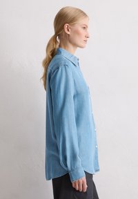 Jasnoniebieska koszula dżinsowa z klasycznym kołnierzykiem, zapinana na guziki, z długimi rękawami. Charakteryzuje się luźnym krojem i lekko zaokrąglonym dołem.