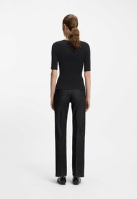 anliegendes, geripptes schwarzes Oberteil mit kurzen Ärmeln, kombiniert mit gerade geschnittenen, dunklen Jeans, die eine glatte Textur und subtile Nähtedetails zeigen.